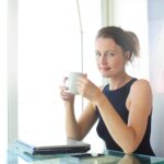 Young woman sitting at her desk, holding a coffee cup and smiling. Ideal for workplace and lifestyle themes.